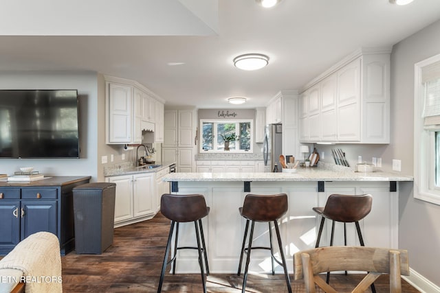 kitchen with a sink, blue cabinetry, a peninsula, white cabinetry, and stainless steel refrigerator