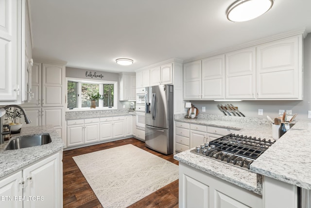 kitchen with white cabinetry, light stone countertops, stainless steel appliances, and a sink
