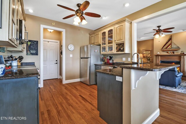 kitchen with wood finished floors, glass insert cabinets, freestanding refrigerator, a kitchen bar, and a ceiling fan