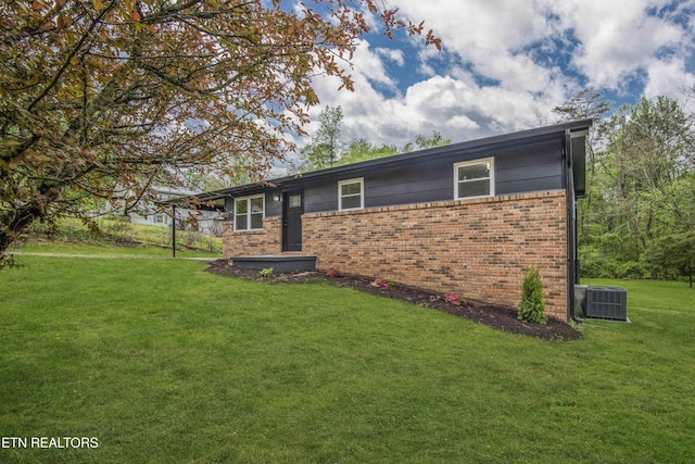 exterior space with central AC unit, brick siding, and a front lawn