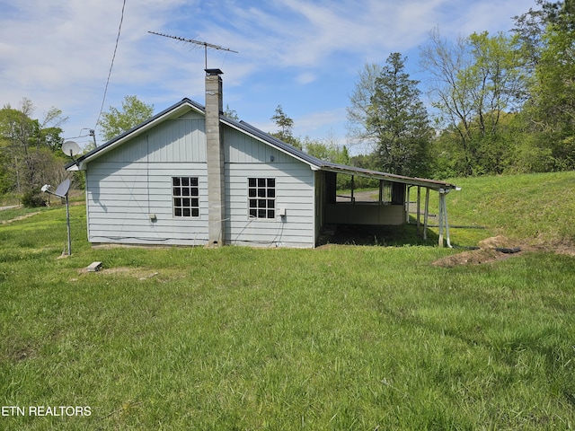 rear view of property with a lawn, a carport, and a chimney