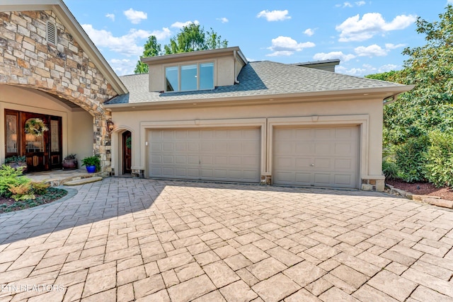 view of front of property with a garage, stone siding, decorative driveway, stucco siding, and a shingled roof