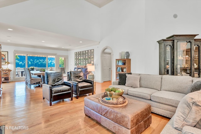living area featuring arched walkways, light wood-type flooring, a high ceiling, ornamental molding, and recessed lighting