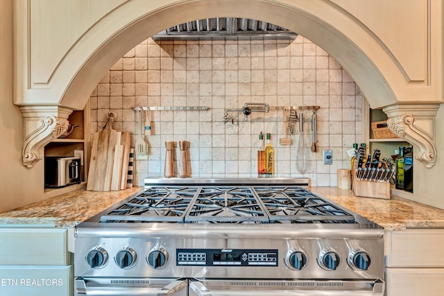 kitchen with stainless steel range with gas stovetop, tasteful backsplash, open shelves, light stone countertops, and arched walkways