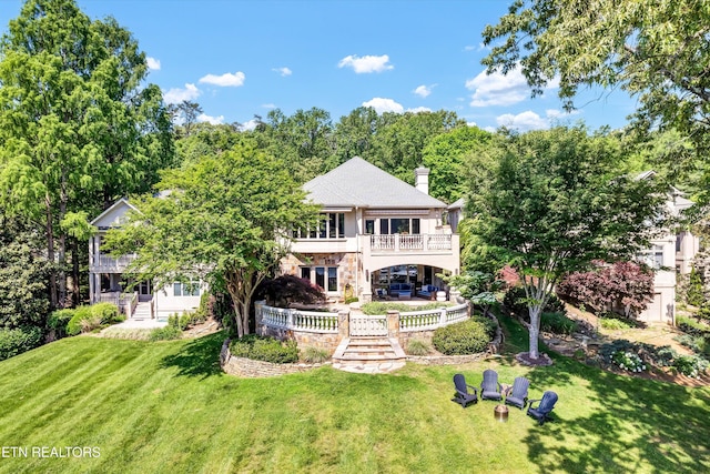 back of house with a chimney, a yard, stone siding, and a balcony