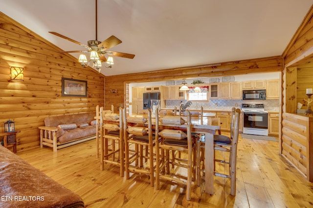 dining space with rustic walls, vaulted ceiling, light wood-style flooring, and a ceiling fan