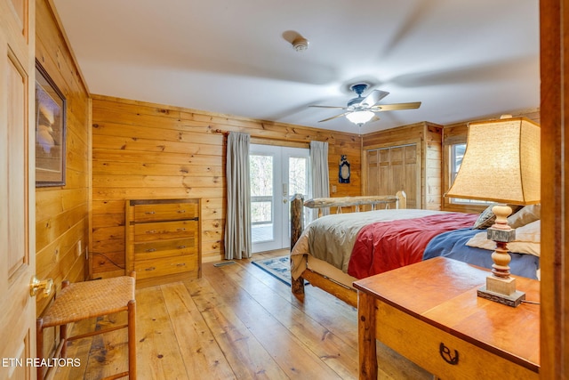 bedroom featuring light wood finished floors, a ceiling fan, wood walls, and access to outside
