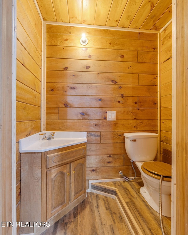 half bathroom featuring wood finished floors, vanity, wooden walls, wood ceiling, and toilet