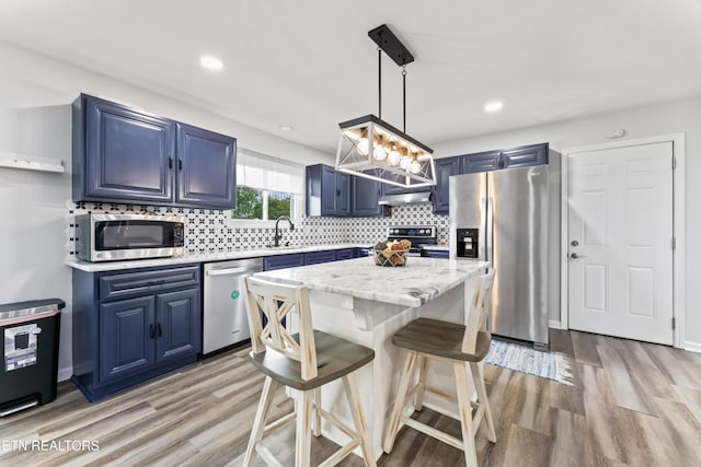 kitchen featuring a breakfast bar, stainless steel appliances, light wood finished floors, blue cabinetry, and backsplash