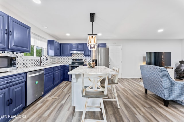 kitchen with stainless steel appliances, a breakfast bar, a sink, tasteful backsplash, and blue cabinetry
