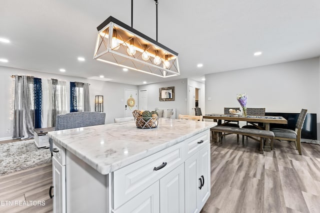 kitchen featuring recessed lighting, light wood-style floors, light stone countertops, a kitchen island, and white cabinetry