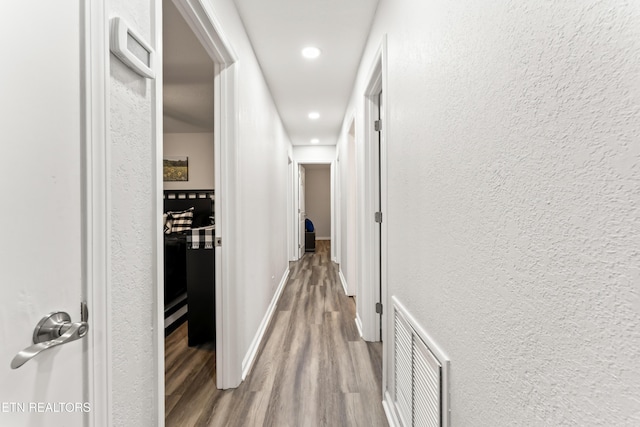 corridor with wood finished floors, a textured wall, baseboards, visible vents, and recessed lighting
