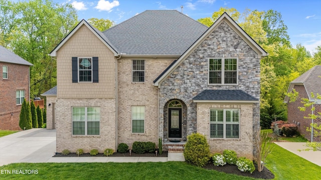 view of front facade with a front yard, a shingled roof, and brick siding