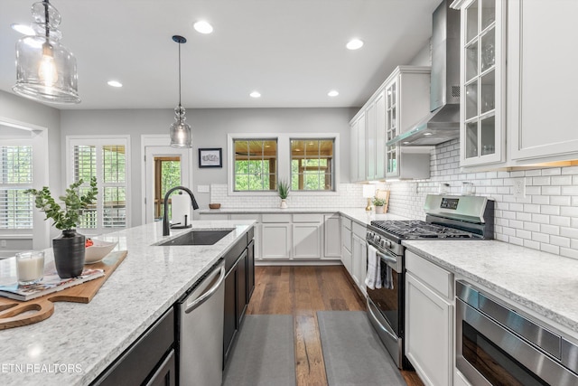 kitchen featuring a sink, dark wood-type flooring, wall chimney exhaust hood, white cabinets, and appliances with stainless steel finishes