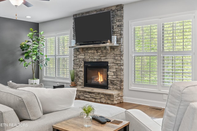 living area featuring wood finished floors, ceiling fan, a fireplace, baseboards, and visible vents