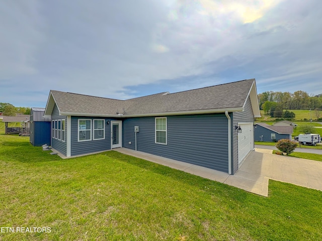 rear view of property featuring a shingled roof, driveway, a yard, and an attached garage