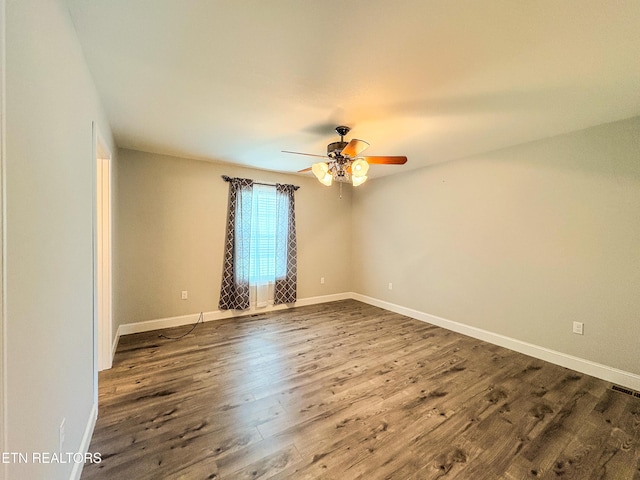 spare room featuring dark wood-style flooring, a ceiling fan, and baseboards