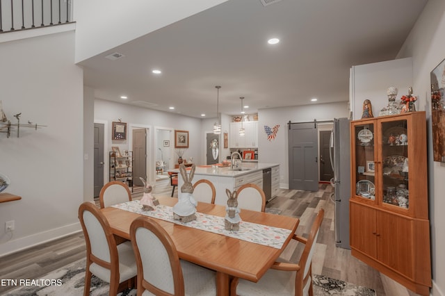 dining room with a barn door, light wood-style flooring, baseboards, visible vents, and recessed lighting