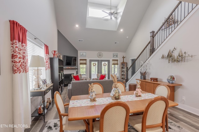 dining room with high vaulted ceiling, stairs, a skylight, light wood finished floors, and visible vents