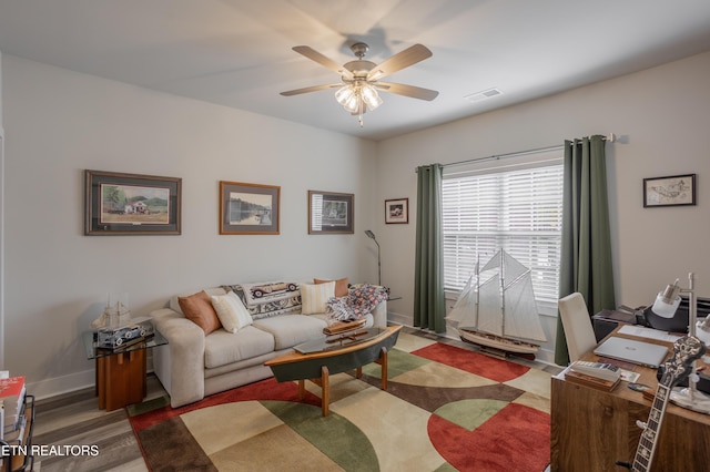 living area with wood finished floors, visible vents, baseboards, and ceiling fan