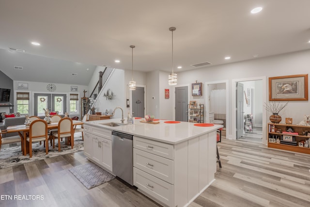 kitchen with stainless steel dishwasher, a sink, open floor plan, visible vents, and white cabinetry