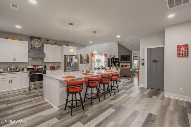 kitchen featuring a kitchen breakfast bar, visible vents, white cabinetry, appliances with stainless steel finishes, and premium range hood