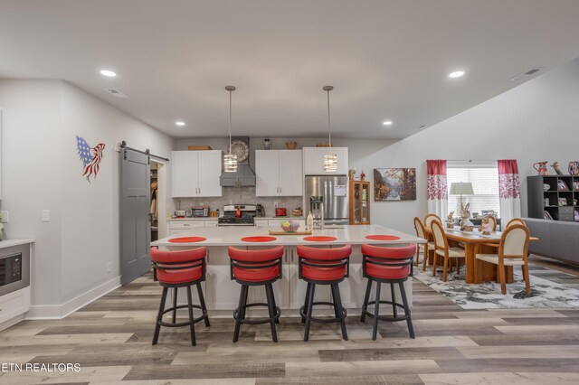 kitchen with a barn door, light wood finished floors, custom range hood, appliances with stainless steel finishes, and visible vents
