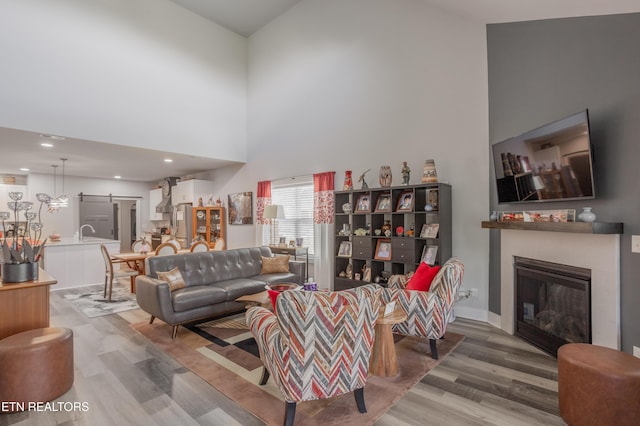 living room featuring a barn door, a high ceiling, a glass covered fireplace, and light wood finished floors