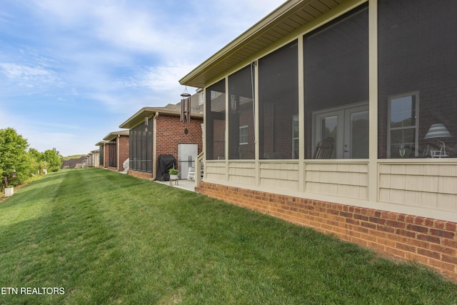 view of side of property with brick siding, a sunroom, and a lawn