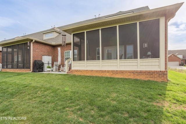 back of house with brick siding, a sunroom, a shingled roof, and a lawn