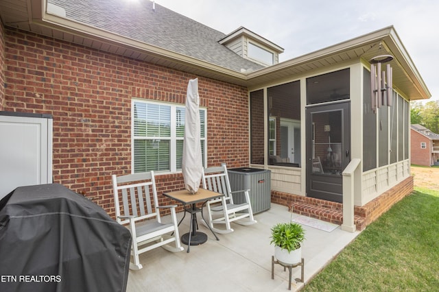 back of house featuring central AC unit, a patio area, a shingled roof, brick siding, and a sunroom