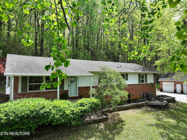 ranch-style home featuring central AC unit, a detached garage, an outbuilding, a front yard, and brick siding