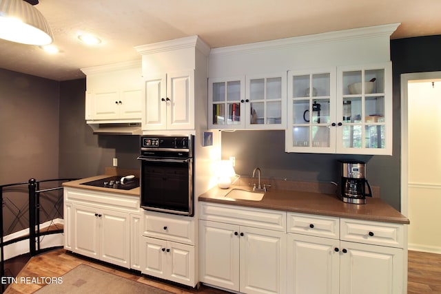 kitchen featuring black appliances, wood finished floors, a sink, and glass insert cabinets
