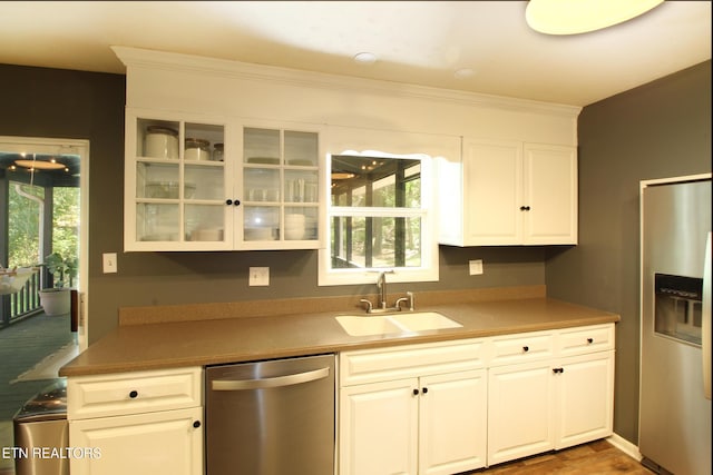 kitchen featuring a sink, glass insert cabinets, stainless steel appliances, white cabinetry, and ornamental molding