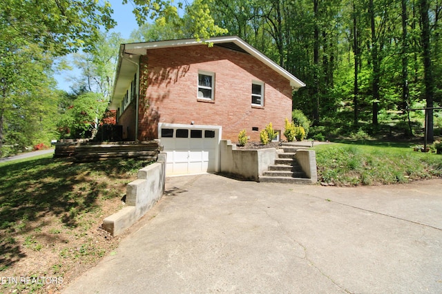 view of side of home featuring brick siding, a garage, aphalt driveway, and stairs