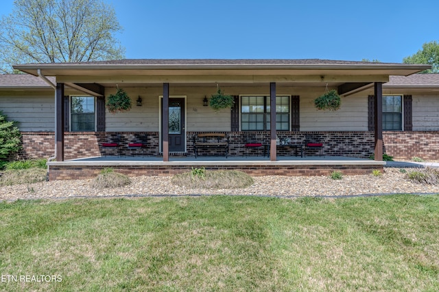view of front facade with covered porch, brick siding, a front yard, and roof with shingles