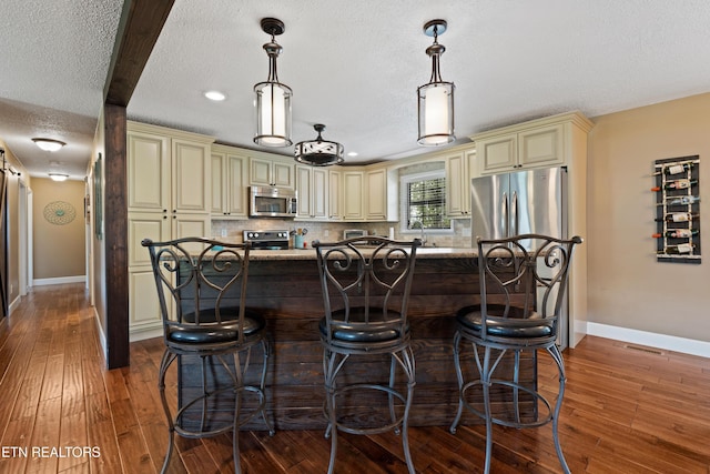 kitchen with baseboards, appliances with stainless steel finishes, hardwood / wood-style floors, and cream cabinetry