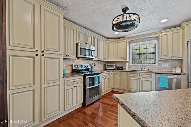 kitchen with cream cabinets, a textured ceiling, a sink, and stainless steel appliances