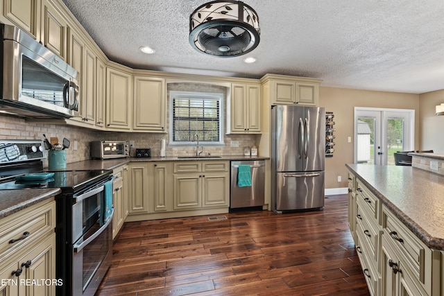 kitchen featuring appliances with stainless steel finishes, a textured ceiling, cream cabinets, and a sink