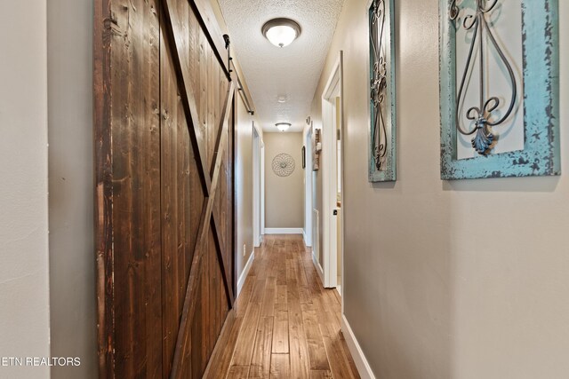 corridor featuring hardwood / wood-style floors, a barn door, a textured ceiling, and baseboards