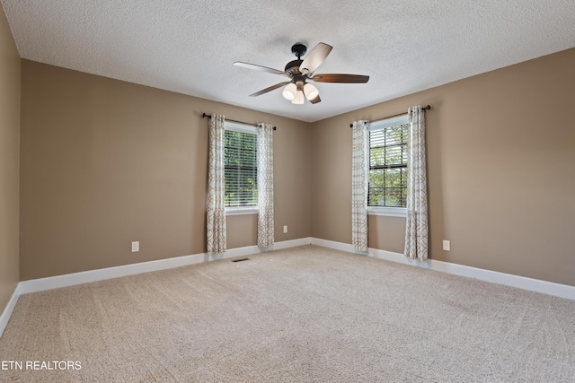 empty room featuring a textured ceiling, light colored carpet, a ceiling fan, and baseboards