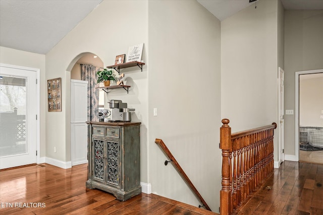 corridor with arched walkways, hardwood / wood-style floors, high vaulted ceiling, and an upstairs landing