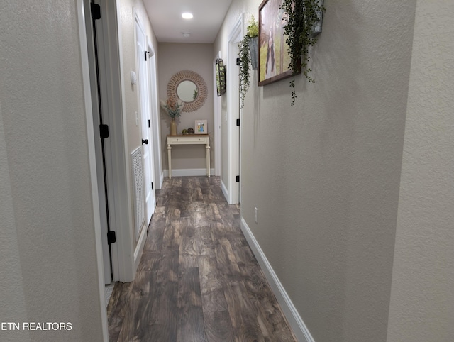 corridor with visible vents, a textured wall, baseboards, and dark wood finished floors