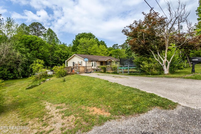ranch-style house featuring a wooden deck, a trampoline, a front lawn, and aphalt driveway
