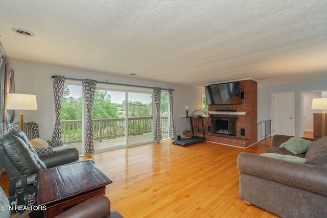 living room featuring a textured ceiling, visible vents, light wood-style flooring, and a fireplace