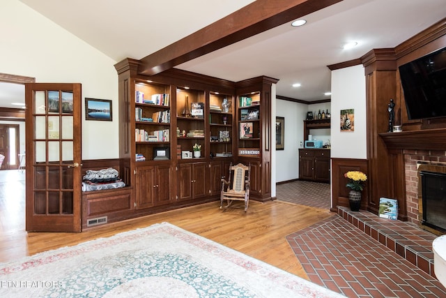 sitting room with a brick fireplace, light wood finished floors, visible vents, and crown molding