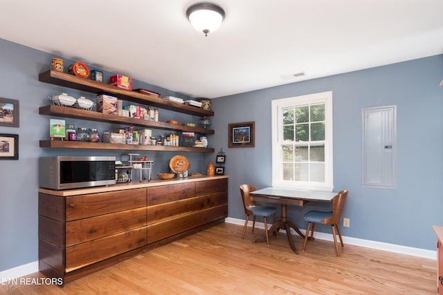 bar with stainless steel microwave, visible vents, electric panel, baseboards, and light wood-type flooring