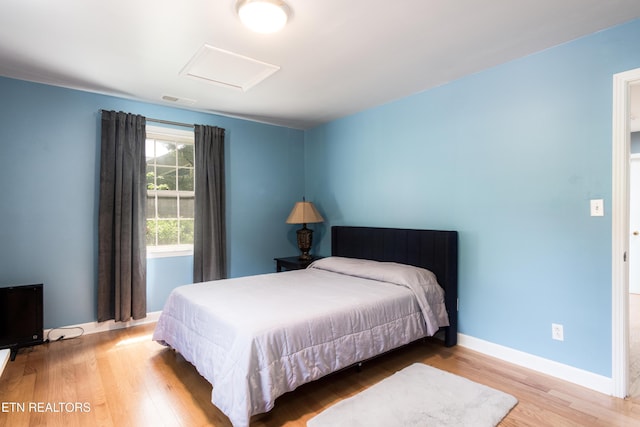 bedroom with baseboards, visible vents, attic access, and wood finished floors