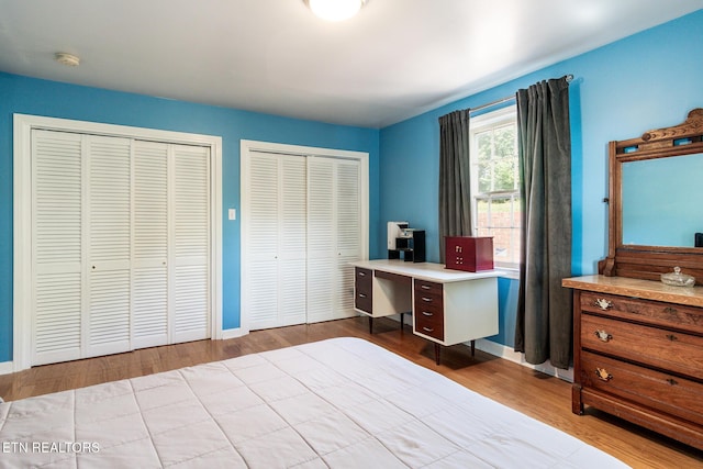 bedroom with wood finished floors, multiple closets, and baseboards