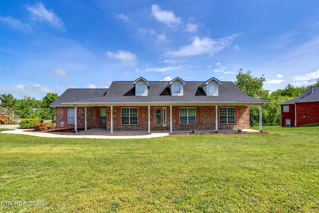 view of front of house featuring a front lawn, a porch, a shingled roof, and brick siding